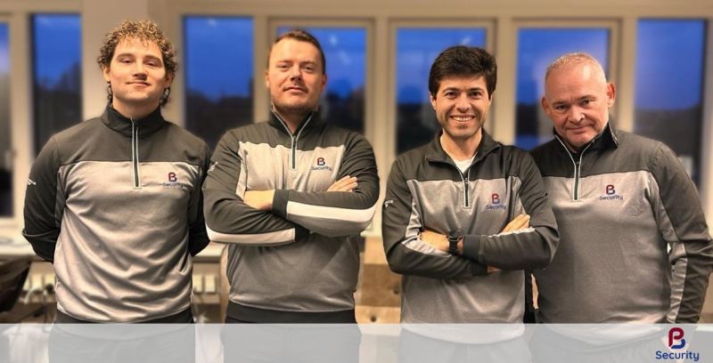 Four members of the PB Security team in branded jackets, standing together in front of a row of windows at dusk