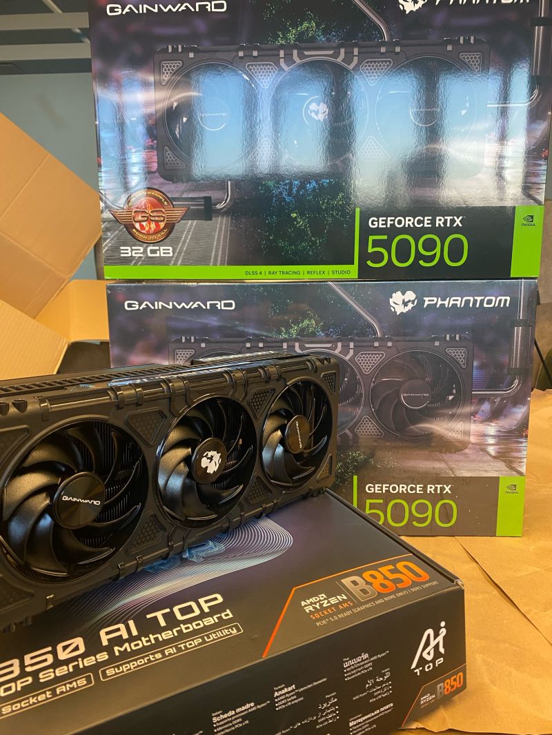 Two boxed Gainward Phantom GeForce RTX 5090 cards with 32 GB each, one card unboxed in front of them, and an AMD Ryzen B850 AI TOP motherboard